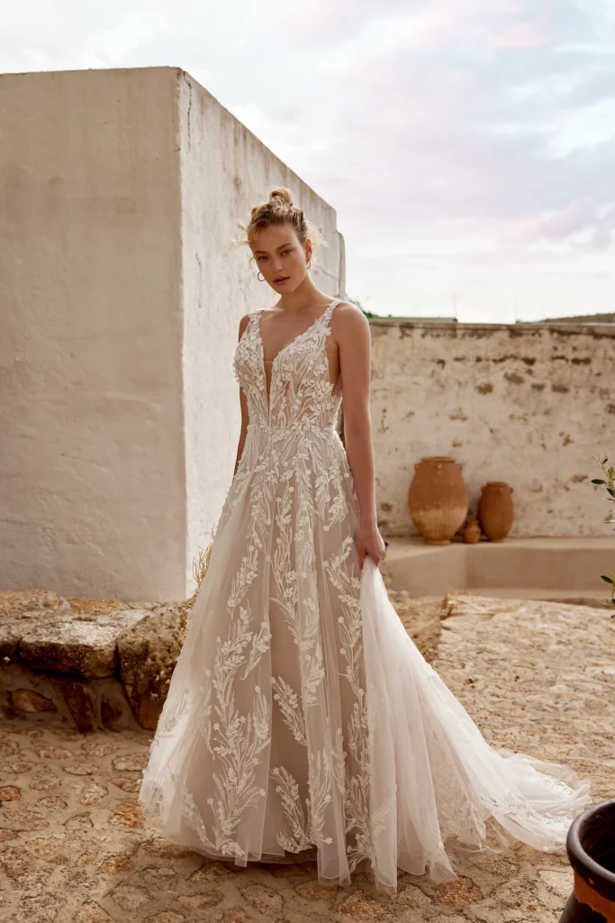 66372-Lillian West-Pure Bridal. Edmonton wedding shop, Edmonton bridal shop, Edmonton wedding dress.Tulle A-line gown with plunging V-neckline with mesh insert and straps. Adorned with lace embroidery featuring tonal sequins, bubble beads, seed beads and clear crystals throughout. 3-D chiffon leafy appliques trickled throughout the lace embroidery. Features sheer bodice with exposed boning peeking out and mesh V side cut-outs. Plunging V-back with buttons to end of zip. Skirt trails into chapel length train. Version with fully lined bodice available