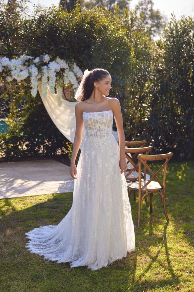 66432-Lillian West-Pure Bridal. Edmonton wedding shop, Edmonton bridal shop, Edmonton wedding dress.Allover chantilly lace A-line gown with a strapless cat eye neckline. Sheer bodice reveals a layer of chantilly lace and exposed boning under matte lace and 3D tonal beaded lace appliques. Bodice is finished with soft draping. Lace appliques trickle down the slight basque waistline and into the skirt. Back bodice is finished with a lace up corset detail. Complete with a chapel length train featuring a scalloped eyelash hem. Version with fully lined bodice available as 66432LND. Version with zipper back available as 66432Z