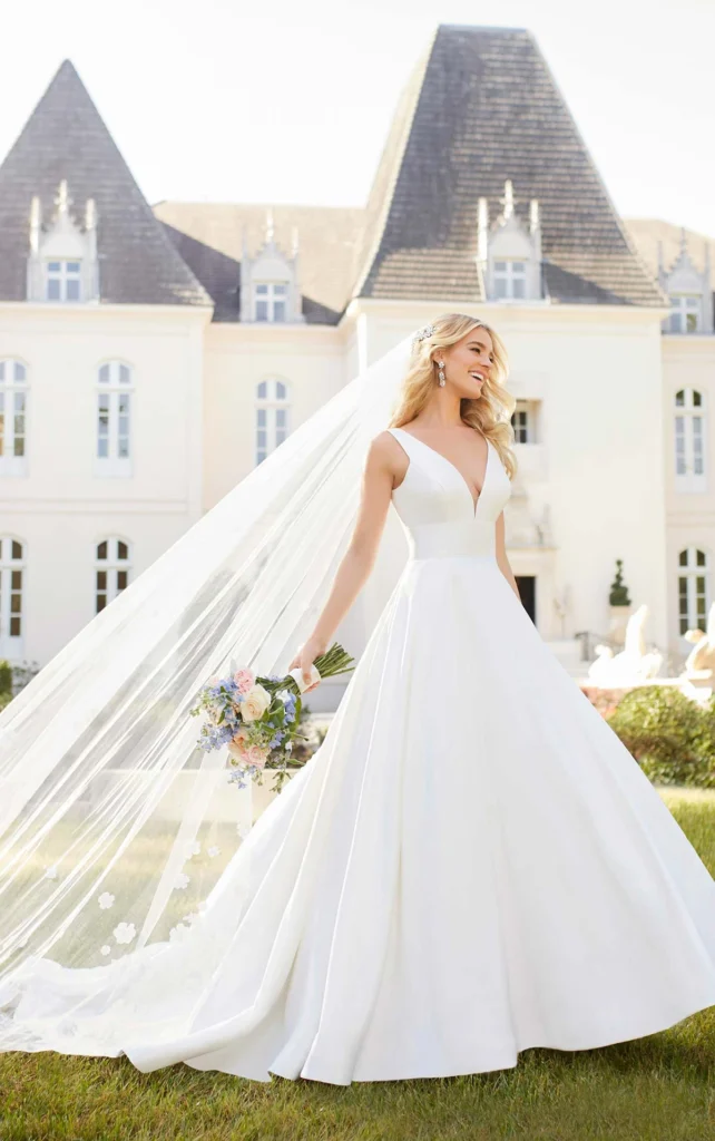 Style 6758 Timeless Stella York royal-inspired wedding dress at Pure Bridal Edmonton featuring a matte Mikado ballgown silhouette, deep V-neckline, empire waist, open square back, long cathedral veil, fabric-covered buttons, available in plus sizes at Pure Bridal Edmonton bridal boutique.