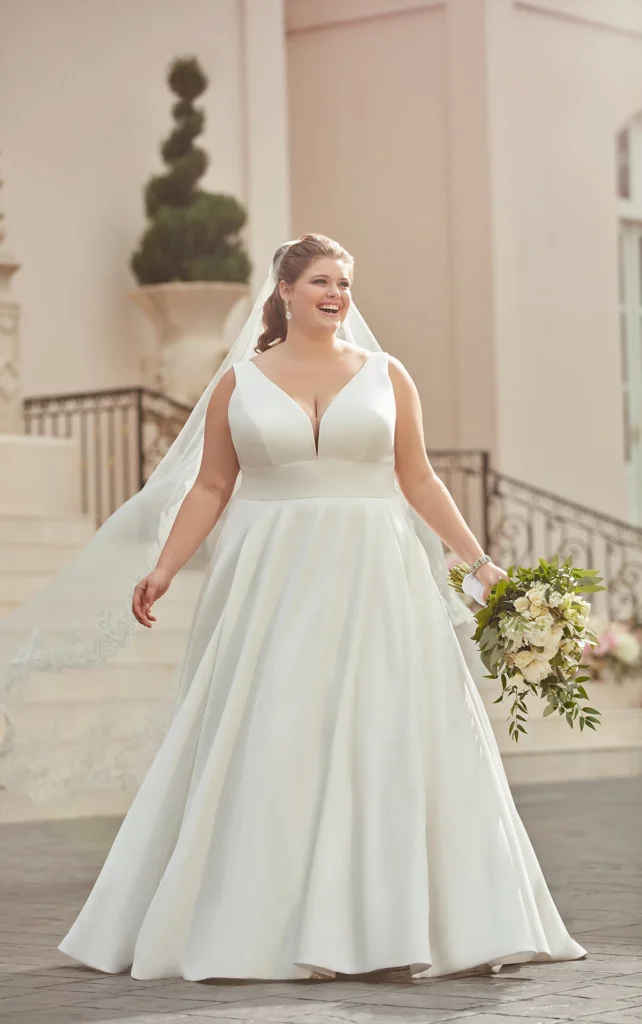 Style 6758 Timeless Stella York royal-inspired wedding dress at Pure Bridal Edmonton featuring a matte Mikado ballgown silhouette, deep V-neckline, empire waist, open square back, long cathedral veil, fabric-covered buttons, available in plus sizes at Pure Bridal Edmonton bridal boutique.