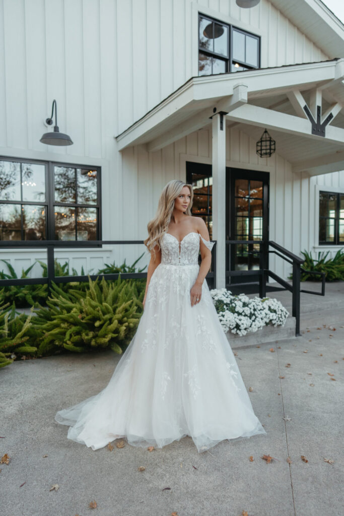 7849-Stella York-Pure Bridal, ROMANTIC LACE AND TULLE OFF-THE-SHOULDER A-LINE WEDDING DRESS This dreamy off-the-shoulder lace wedding dress artfully blends timeless romance with fashion-forward design. Style 7849 features romantic off-the-shoulder detachable straps in an ethereal leafy lace floral to match the fitted corset-style bodice with a daring plunging sweetheart neckline. Brides can choose between a lined or sheer lace bodice for customizable glamour. Embellished florals trail past the waist into delicate vines before scattering across the frothy A-line skirt in shimmering layers of glitter tulle. Both charming and refined, this sweetheart off-the-shoulder wedding gown is an absolute vision down the aisle. This wedding gown is also available in plus sizes, Edmonton wedding shop, Edmonton wedding dress