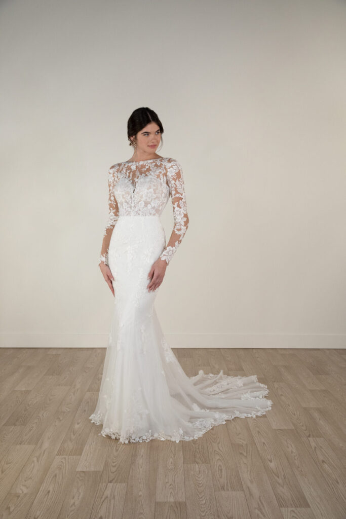 Stella York-7867-Pure Bridal-Edmonton Bridal Shop-Wedding dress-sleeves-lace, ROMANTIC FIT-AND-FLARE WEDDING DRESS WITH LONG LACE SLEEVES For an unforgettable wedding day look, Style 7867’s sexy fit-and-flare long-sleeve wedding dress is a design for the romantic bride. Gorgeous optional matte lace paints the skin in delicate florals with a sheer high neckline and elegant long sleeves. Beneath the illusion lies a sexy sweetheart neckline and fitted bodice with a low V-back scoop and a small row of fabric-covered buttons in the back. The stunning fit-and-flare silhouette graces every curve of the body, with 3D floral and lace appliqués exquisitely placed to create a daring and sophisticated bridal look. This gown is available with or without glitter tulle and beading.