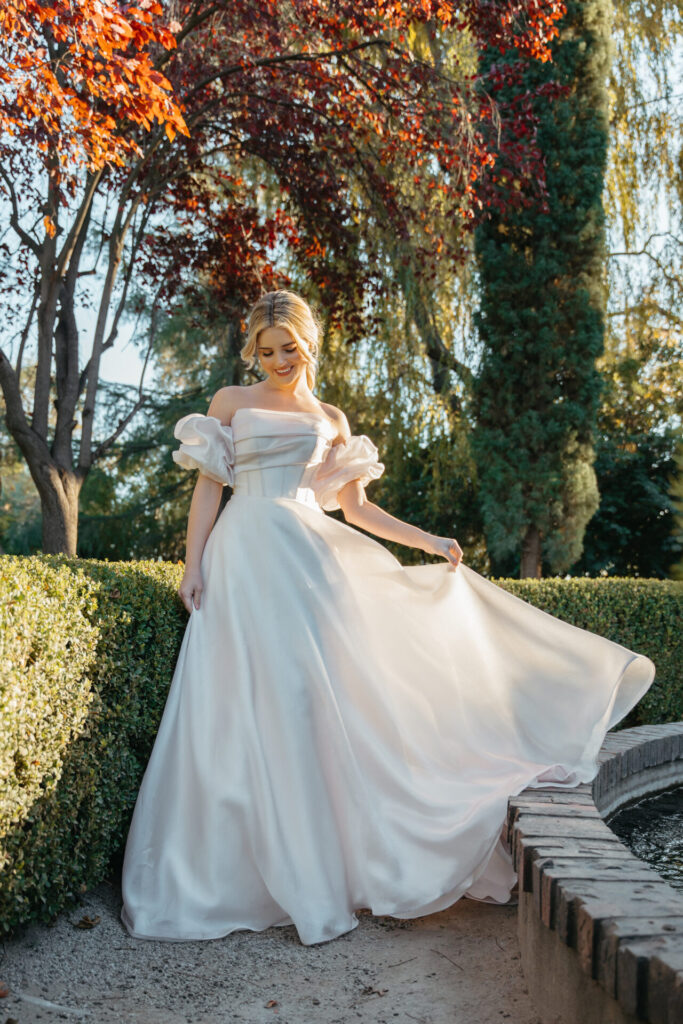 7940-Stella York-Pure Bridal, PRINCESS PUFF SLEEVE ORGANZA BALLGOWN WEDDING DRESS Style 7940 is an on-trend puffy sleeve wedding gown that exudes pure sophistication and cosmopolitan glamour. The pearl organza ballgown wedding dress features detachable off-the-shoulder puff sleeves that complement the length of the bodice—covering the mid-upper arm to the elbow. A gorgeously draped strapless bodice features a straight across neckline with structured corset boning to support the form and draw the eye to the natural hourglass figure. From the waist, the lustrous pearl organza floats into a romantic princess ballgown skirt, complete with discreet side pockets and a row of fabric-covered buttons down the back. This regal princess ballgown was made for bridal royalty. This wedding gown is also available in plus sizes, Edmonton wedding shop, Edmonton wedding dress