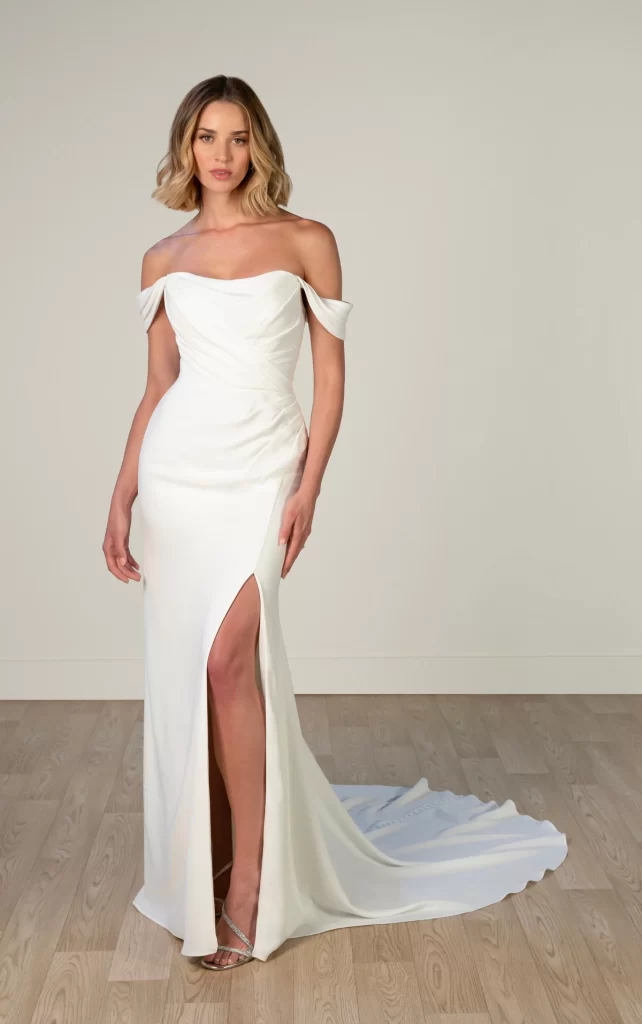 8018-Stella York-Pure Bridal-Edmonton wedding store, Edmonton bridal shop, Edmonton wedding dress, Exuding modern sophistication, this luxe crepe wedding dress embraces a figure-flattering column silhouette thats both timeless and on-trend. Style 8018 features a stunning draped bodice with an elegant scooped neckline as detachable off-the-shoulder straps add a touch of effortless sexiness and glamour. The sumptuous crepe fabric drapes beautifully over every curve as an optional leg slit offers an extra dash of charm for the daring bride. With its clean lines and modern design, this off-the-shoulder wedding gown is an ideal fit for the fashion-forward bride looking for an undeniably chic and irresistibly romantic bridal look. This wedding gown is also available in plus sizes.