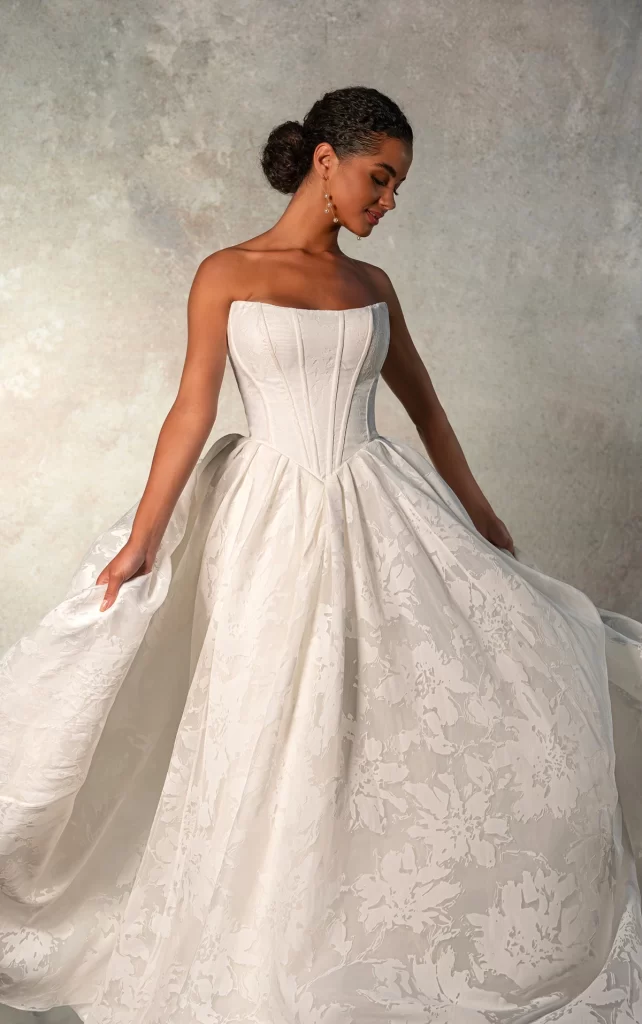 D4158-Essense of Australia-Pure Bridal, Edmonton bridal shop, Edmonton wedding dress.Romantic Princess Strapless Ballgown Wedding Dress with Pockets A modern princess wedding gown comes to life in Style D4158. Featuring a strapless scoop neckline bodice with vertical contouring seams, the fully-lined bodice accentuates the figure while complementing the romantic Basque waist. The back showcases a timeless lace-up detail, adding a touch of old-world charm. From the waist, a full and romantic ballgown skirt billows in a one-of-a-kind textured organza, complete with pockets and long regal train. This enchanting gown beautifully balances modern design with classic bridal elegance for an ultra-romantic ballgown wedding dress made for a fairytale wedding. This wedding gown is also available in plus sizes.