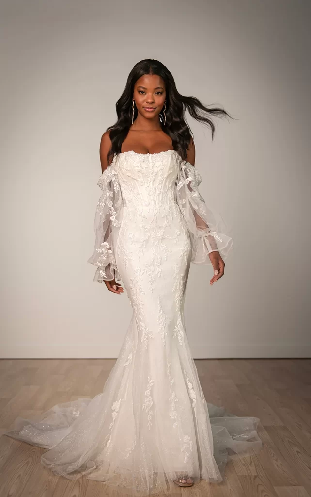 SY8160-Stella York-Pure Bridal. Edmonton wedding shop, Edmonton bridal shop.Step into a world of romance with the ethereal beauty of Style SY8160, a dreamy blend of delicate tulle and romantic Chantilly lace. Detachable off-the-shoulder blouson sleeves float effortlessly, adding a soft, whimsical touch to the corset-inspired bodice with exposed boning and shimmering lace accents. In the back, a row of fabric-covered buttons completes the sheer corset detail, meeting a sleek, fitted skirt that drapes gracefully. With its airy elegance and enchanting design, Style SY8160 is a breathtaking choice for the bride who wants to feel both whimsical and effortlessly sophisticated.