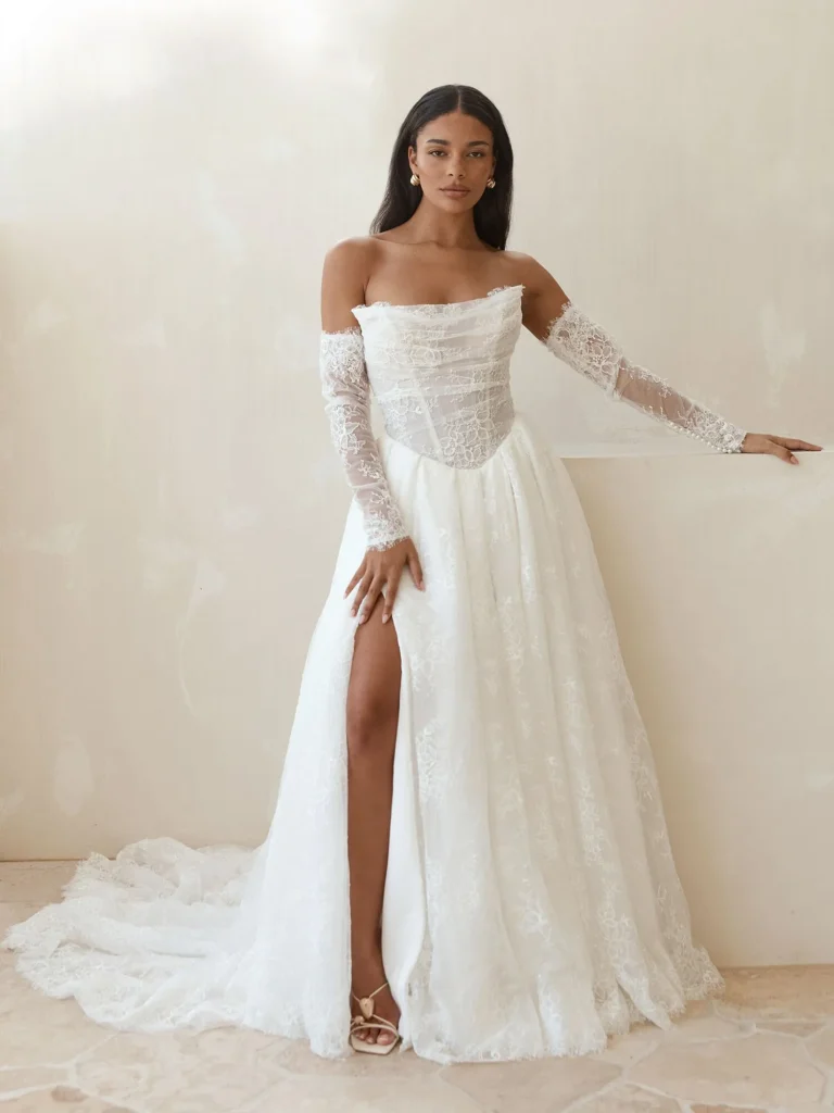 Lilac by Serene by Madi Lane lace A-line wedding dress with a strapless exposed boning bodice, detachable illusion sleeves, and leg split at Pure Bridal in Edmonton.